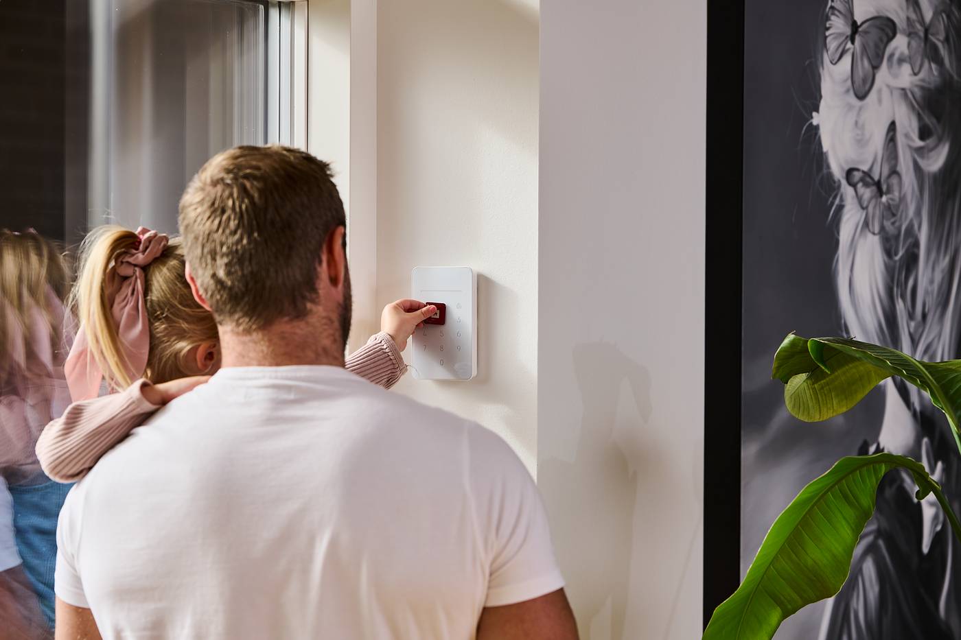 Man med ett barn på armen vid larmets manöverpanel på väggen
