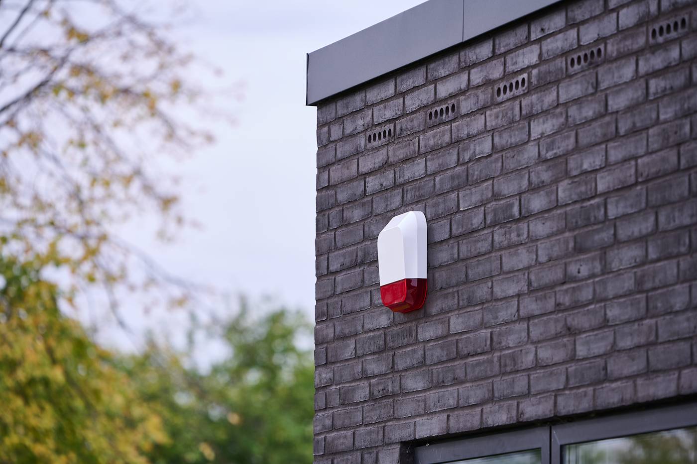 Vit larmsiren med rött blixtljus på en grå tegelfasad