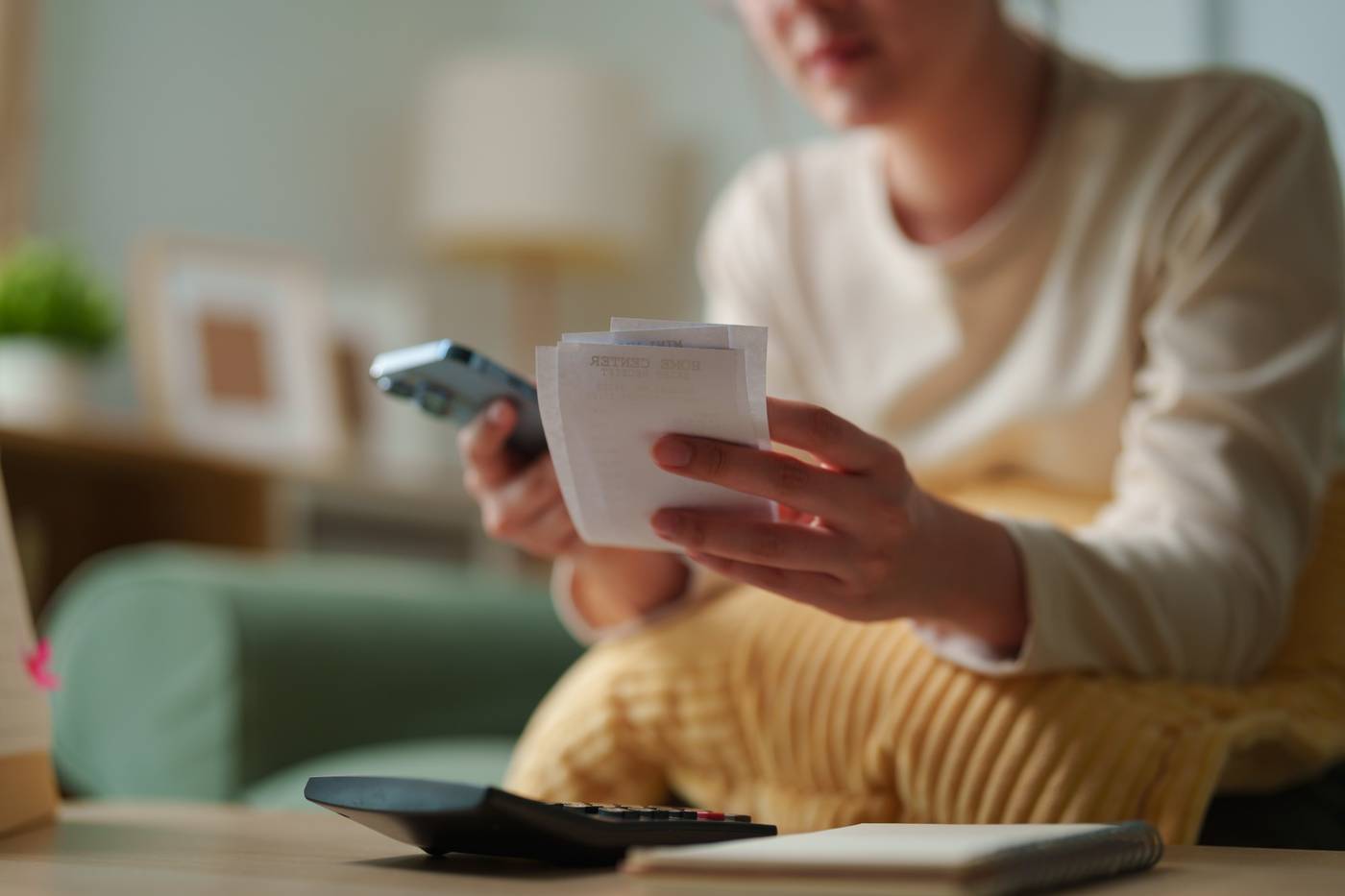 Person i soffan går igenom kvitton med mobil och miniräknare